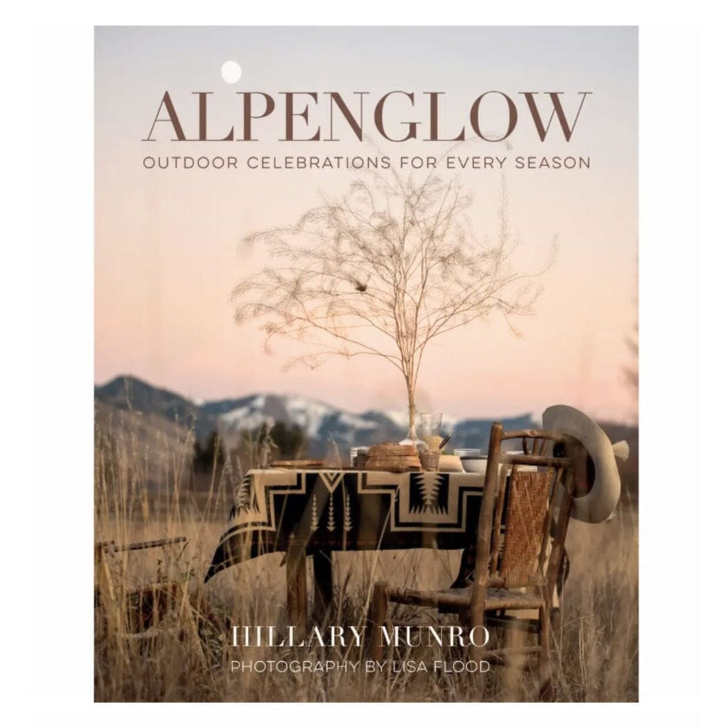Book cover for 'Alpenglow: Outdoor Celebrations for Every Season' by Hillary Munro, featuring a western-themed table and chairs in a mountain landscape at sunset.
