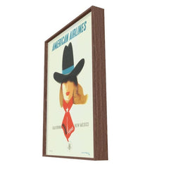 A framed vintage-style American Airlines travel poster shown at an angle against a plain white background. The poster features a woman in a black cowboy hat with a blue band and a red scarf, with the text 'AMERICAN AIRLINES' at the top and 'CALIFORNIA TO NEW MEXICO' near the bottom.