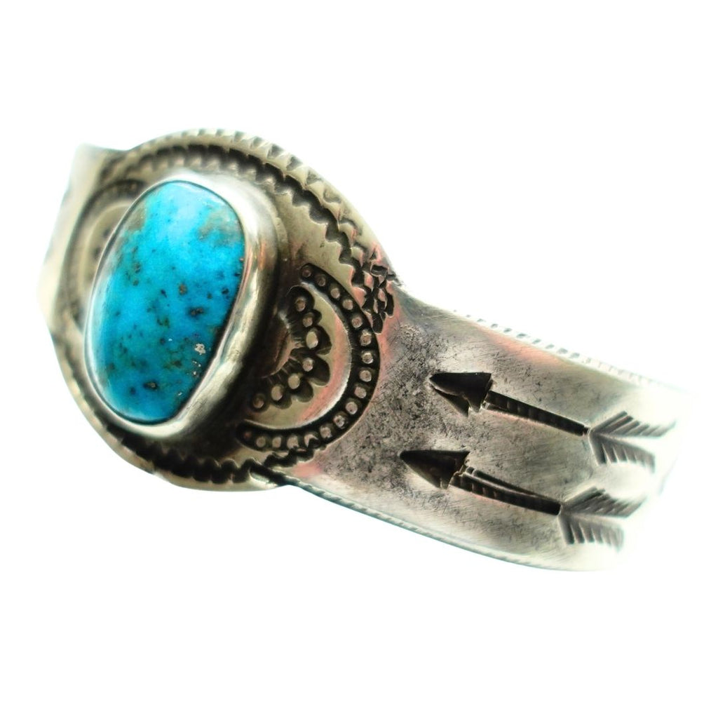 A sterling silver ring featuring a large, oval turquoise cabochon stone with natural inclusions, set in a hand-stamped silver band with arrow and dot patterns.