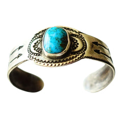 A ingot silver cuff ring featuring a central turquoise cabochon stone with natural matrix inclusions, set against a plain white background.