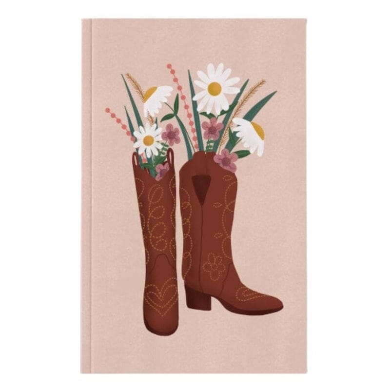 A notebook with a light pink cover notebook featuring an illustration of two brown cowboy boots filled with white daisies and wildflowers, shown against a plain white background.
