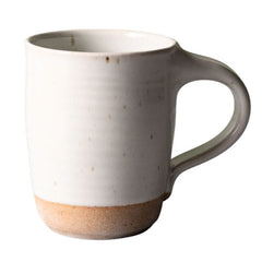 A handmade ceramic mug with a matte off-white glazed body, subtle speckles, and a natural, unglazed sandy beige base.