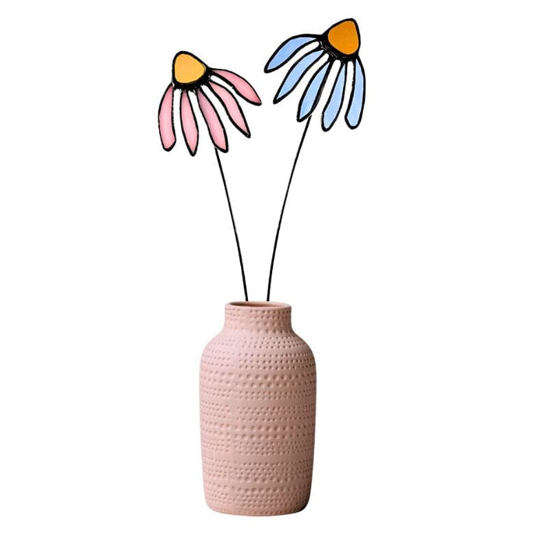 A pink textured ceramic vase holding two stained glass corn flower cutouts with pink and blue petals, black stems, and orange centers, isolated on a white background.