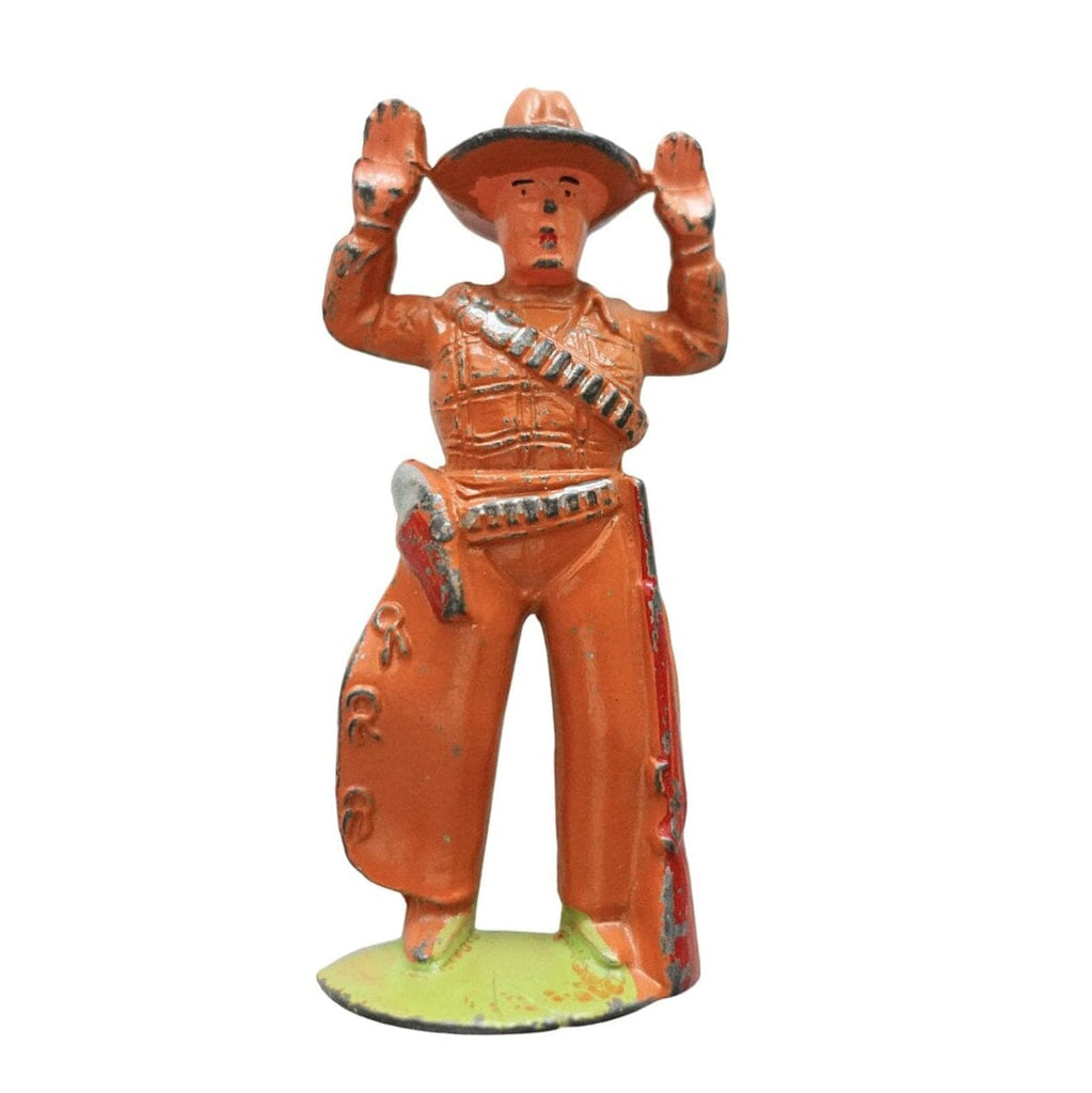 A vintage orange cast iron cowboy figurine with raised hands, standing on a light green base against a white background.