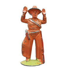 A vintage orange cast iron cowboy figurine with raised hands, standing on a light green base against a white background.