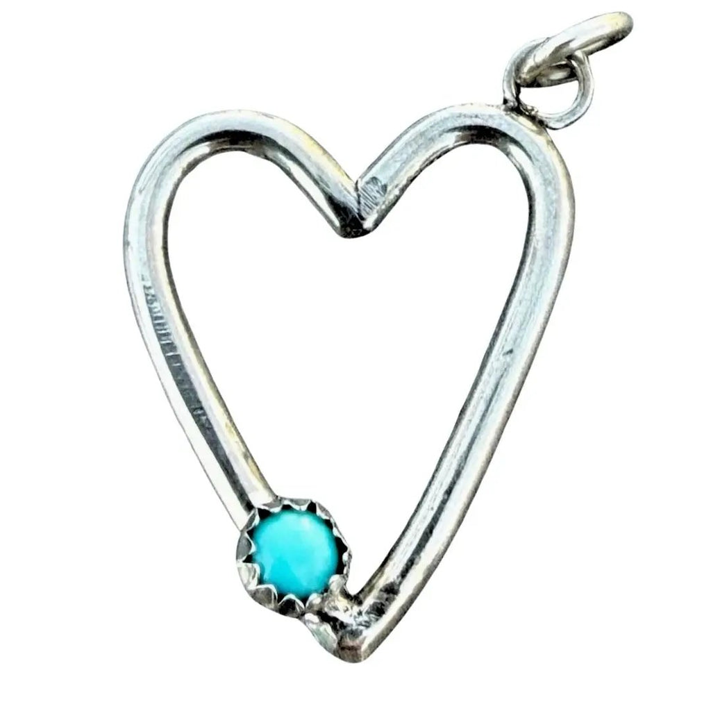 A sterling silver heart-shaped pendant with a small, round turquoise-colored gemstone at the bottom left, set against a plain white background.