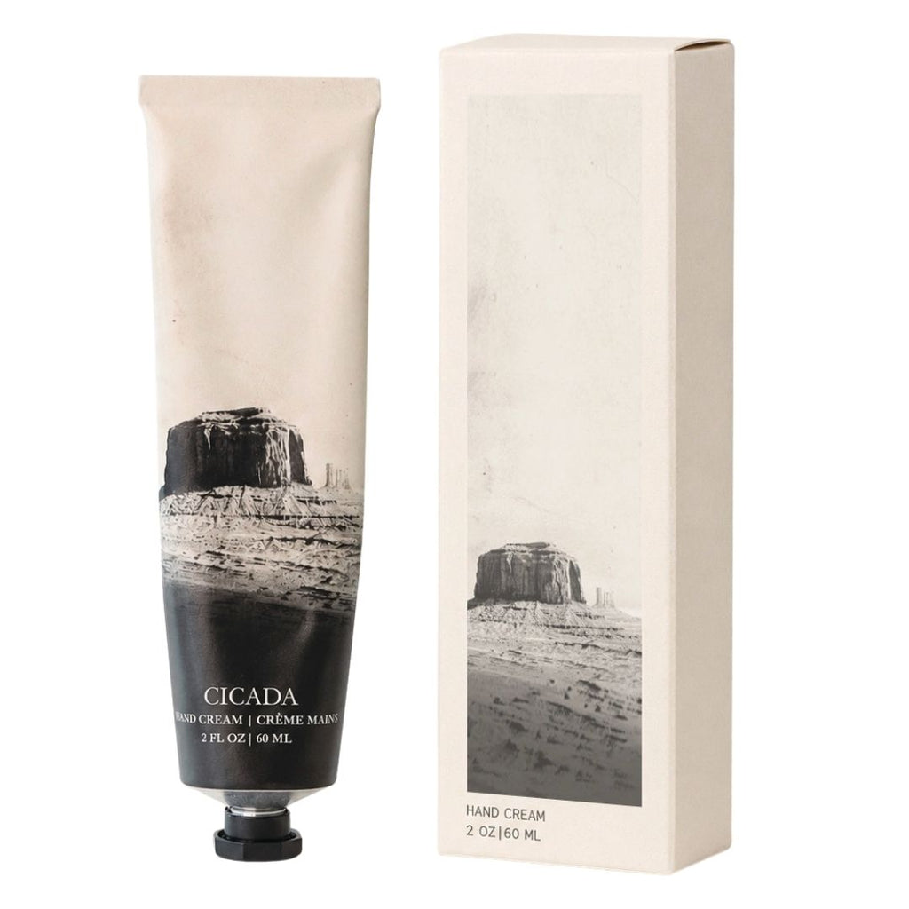 A squeeze tube of Cicada Hand Cream stands next to its matching rectangular box, both featuring a black and white desert rock landscape print on a warm off-white background.
