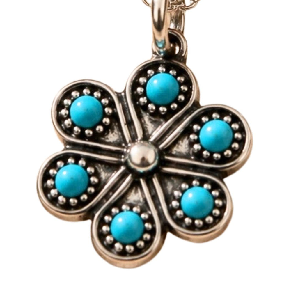 A five-petal flower pendant charm in an antique silver-tone metal, featuring five round turquoise blue cabochon stones set in each petal, with a central silver-tone stone and a bail at the top.