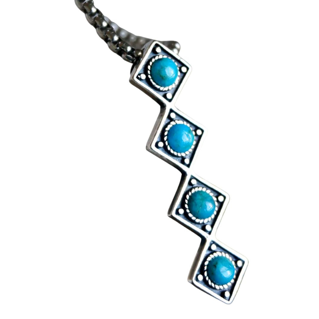 A sterling silver necklace featuring a zigzag pendant with four square links, each set with a round turquoise cabochon stone, shown against a plain white background.