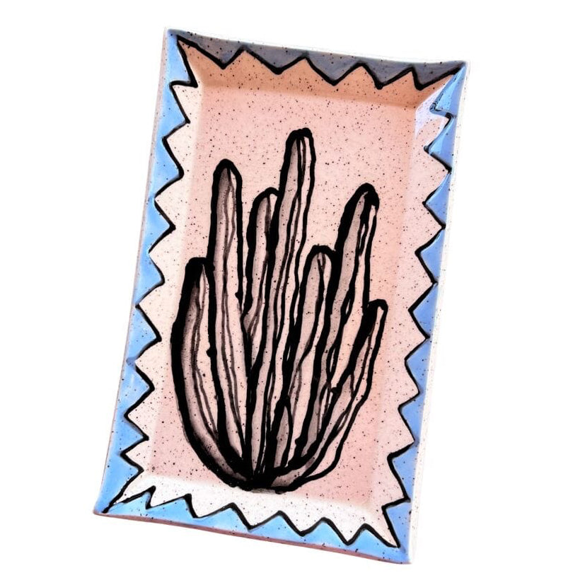 A rectangular ceramic tray with a hand-painted cactus design, featuring a light pink speckled center, a blue border, and a white zigzag outline.