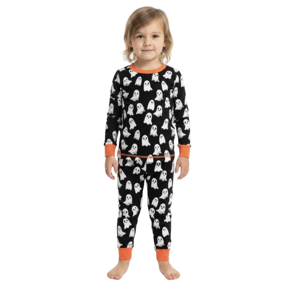 A young child wearing a two-piece Halloween pajama set with a black background, white ghost pattern, and orange trim, standing against a plain white background.
