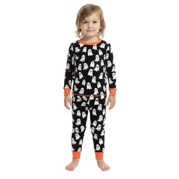 A young child wearing a two-piece Halloween pajama set with a black background, white ghost pattern, and orange trim, standing against a plain white background.