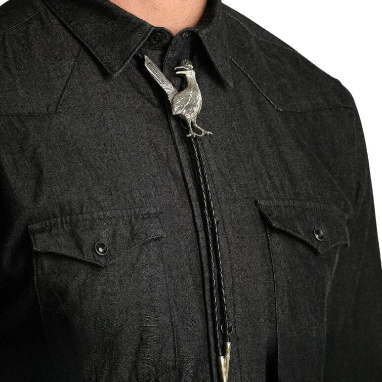 Close-up of a person wearing a black western-style collared shirt with a silver roadrunner bolo tie