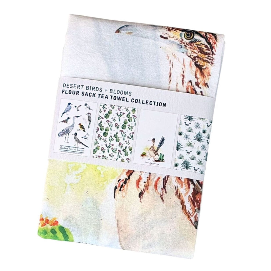 A folded fabric towel with Roadrunner bird and floral watercolor illustrations, wrapped in a paper band labeled 'DESERT BIRDS + BLOOMS FLOUR SACK TEA TOWEL COLLECTION'.