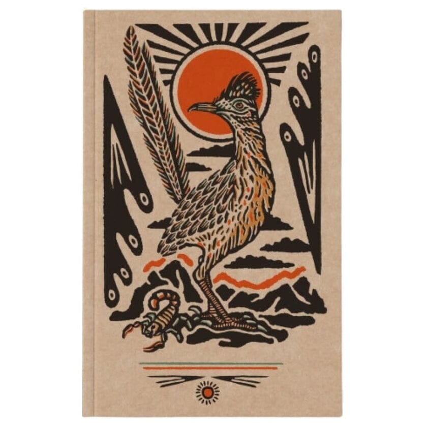 A hardcover notebook with a tan cover featuring a stylized woodcut-style illustration of a roadrunner, a sun, mountains, and a scorpion.
