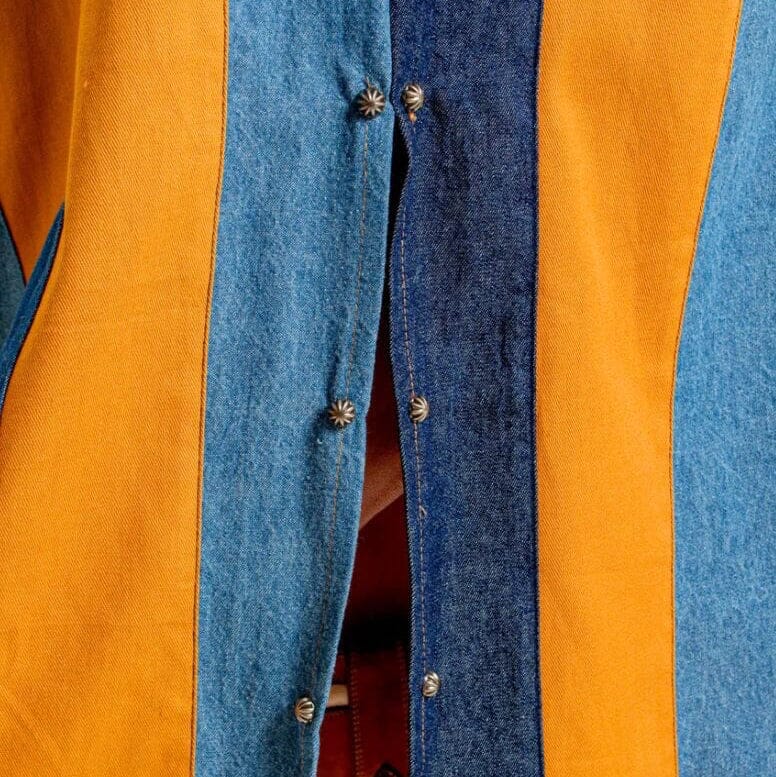Close-up of a button-front garment with wide vertical panels in camel brown and two shades of blue denim, including a central darker blue denim stripe.