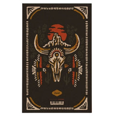 A rectangular dark brown rug with a central Native American-inspired design featuring a skull, curved horns, cacti, geometric borders, and an orange-red sun motif. The brand name 'Dusk' is printed near the bottom center.