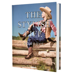 A hardcover book titled 'THE STYLISH LIFE COWBOYS' featuring a cover photo of a woman in cowboy attire sitting on a wooden fence under a blue sky.