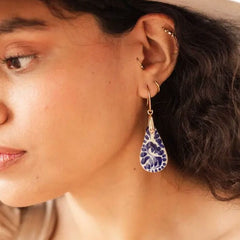 A close-up of a woman wearing a  dangling Talavera teardrop-shaped earring in blue and white floral mosaic.