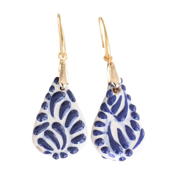 A pair of handmade Talavera teardrop dangle earrings featuring a white clay body with a blue hand-painted floral pattern, suspended from gold French hook ear wires, shown against a plain white background.