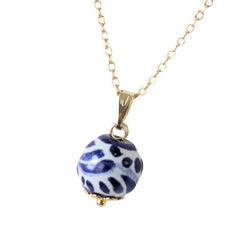 A gold chain necklace featuring a round, Talavera blue and white patterned bead pendant with a small gold cap at the bottom, shown against a plain white background.