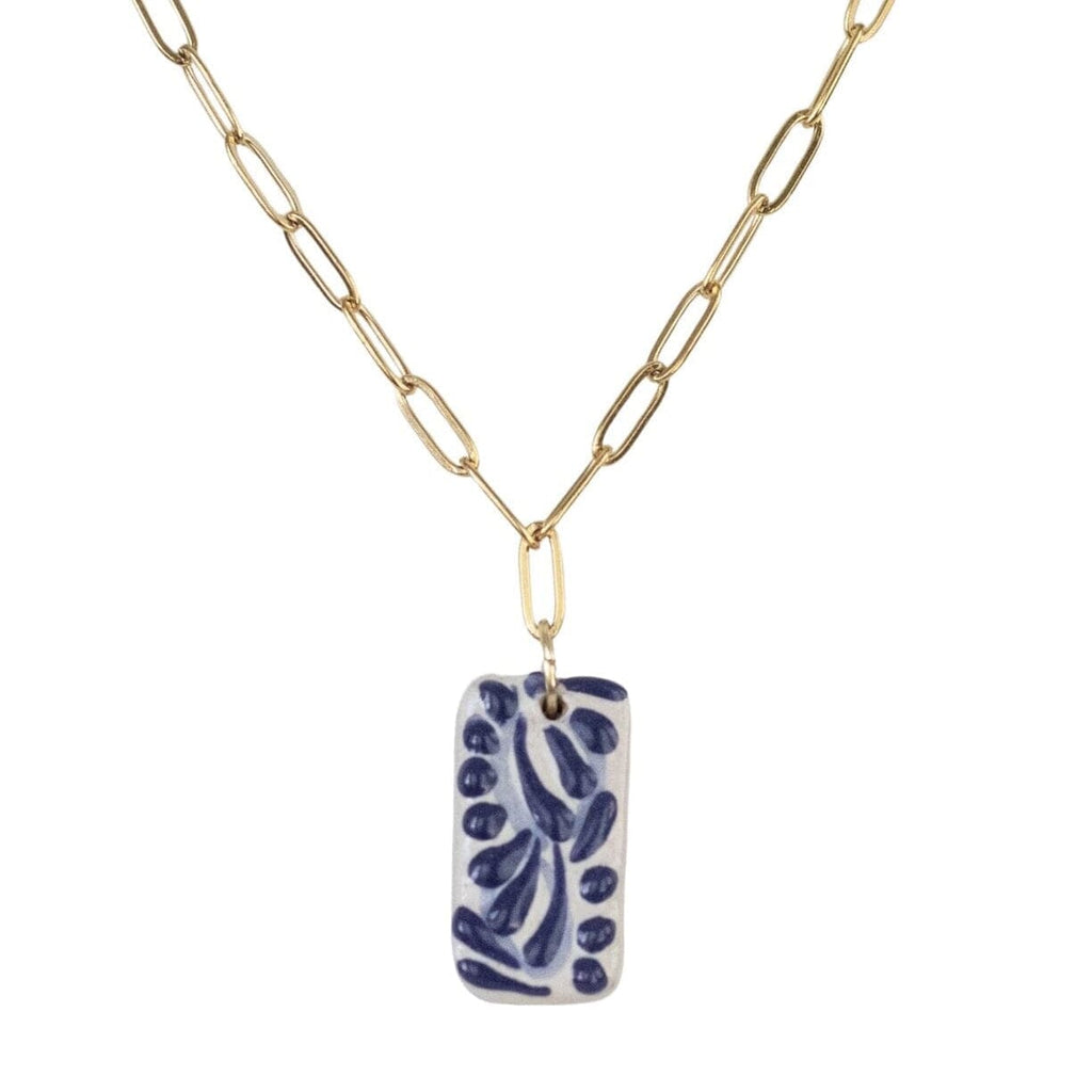 A gold paperclip chain necklace with a rectangular ceramic pendant of Talavera featuring a blue and white leaf pattern, shown on a plain white background.