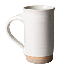 A tall, cylindrical ceramic mug with a C-shaped handle, featuring a glossy off-white glaze and a rustic, unglazed sandy beige base, shown against a plain white background.
