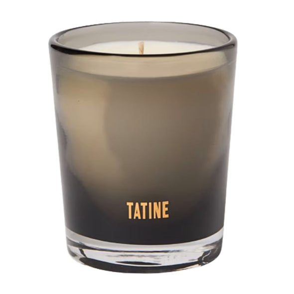 A Tatine brand scented candle in a smoky translucent glass jar with a single wick, shown against a plain white background.