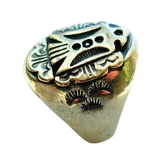 A vintage-style signet ring with a textured, antiqued gold-toned metal face featuring a stylized face motif and floral engravings, set against a plain white background.