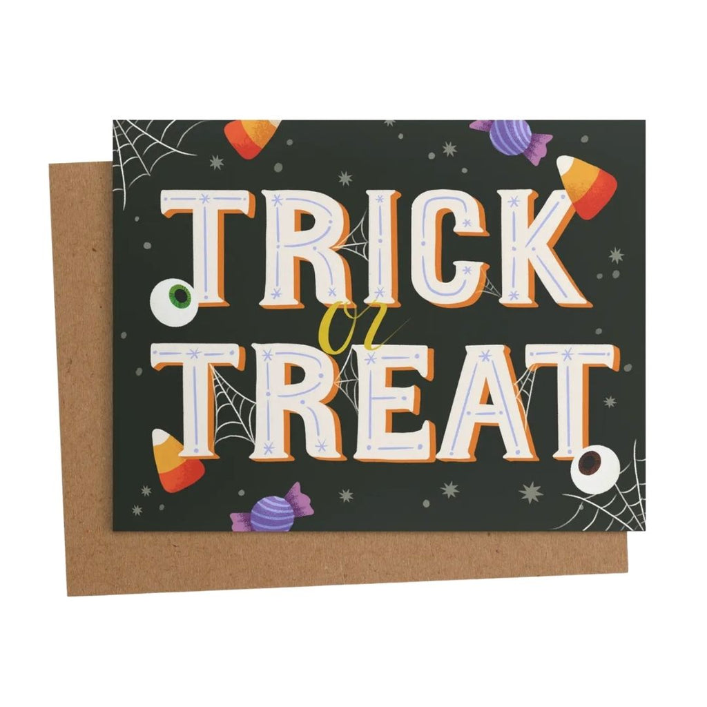 A Halloween greeting card with a brown kraft envelope, featuring the words 'TRICK or TREAT' in large white letters with orange outlines on a dark background decorated with candy corn, spiderwebs, and a purple candy.