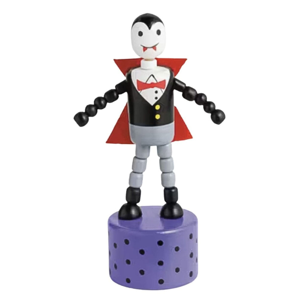 A small vampire toy figurine with a black and white face, black and gray body, red cape, red bow tie, and yellow buttons, standing on a purple perforated cylindrical base against a white background.