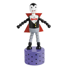A small vampire toy figurine with a black and white face, black and gray body, red cape, red bow tie, and yellow buttons, standing on a purple perforated cylindrical base against a white background.