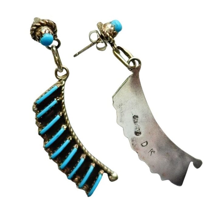 A pair of turquoise dangle earrings by Davis Kaamasee on a plain white background. One earring features a curved gold-toned setting with multiple bright turquoise-blue stones, and the other features a scalloped silver-toned metal charm with his hallmark.